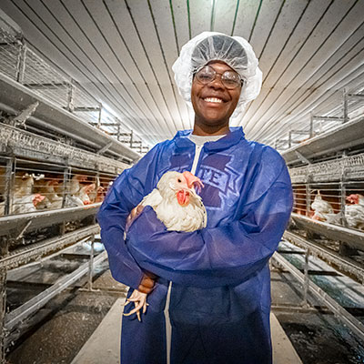 Maryonna Chambers wears a hair net and blue lab coat as she holds a chicken in the poultry house